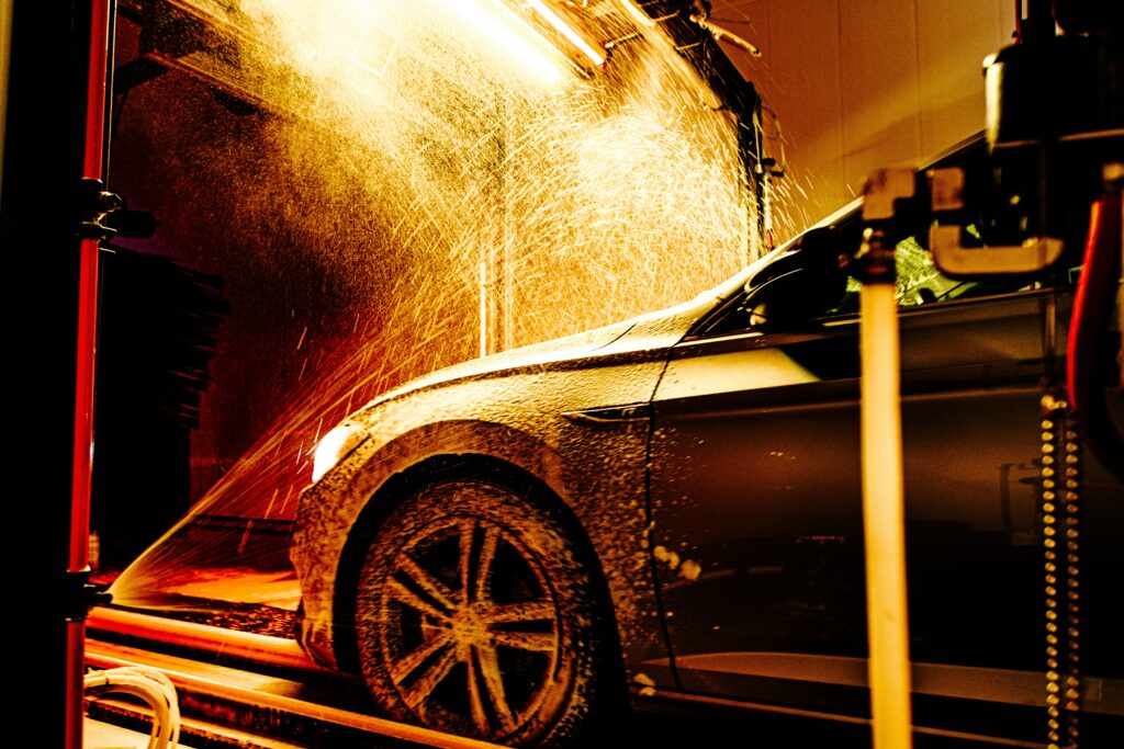 Car going through a car wash tunnel with water spraying from nozzles and blue lighting highlighting the wash process
