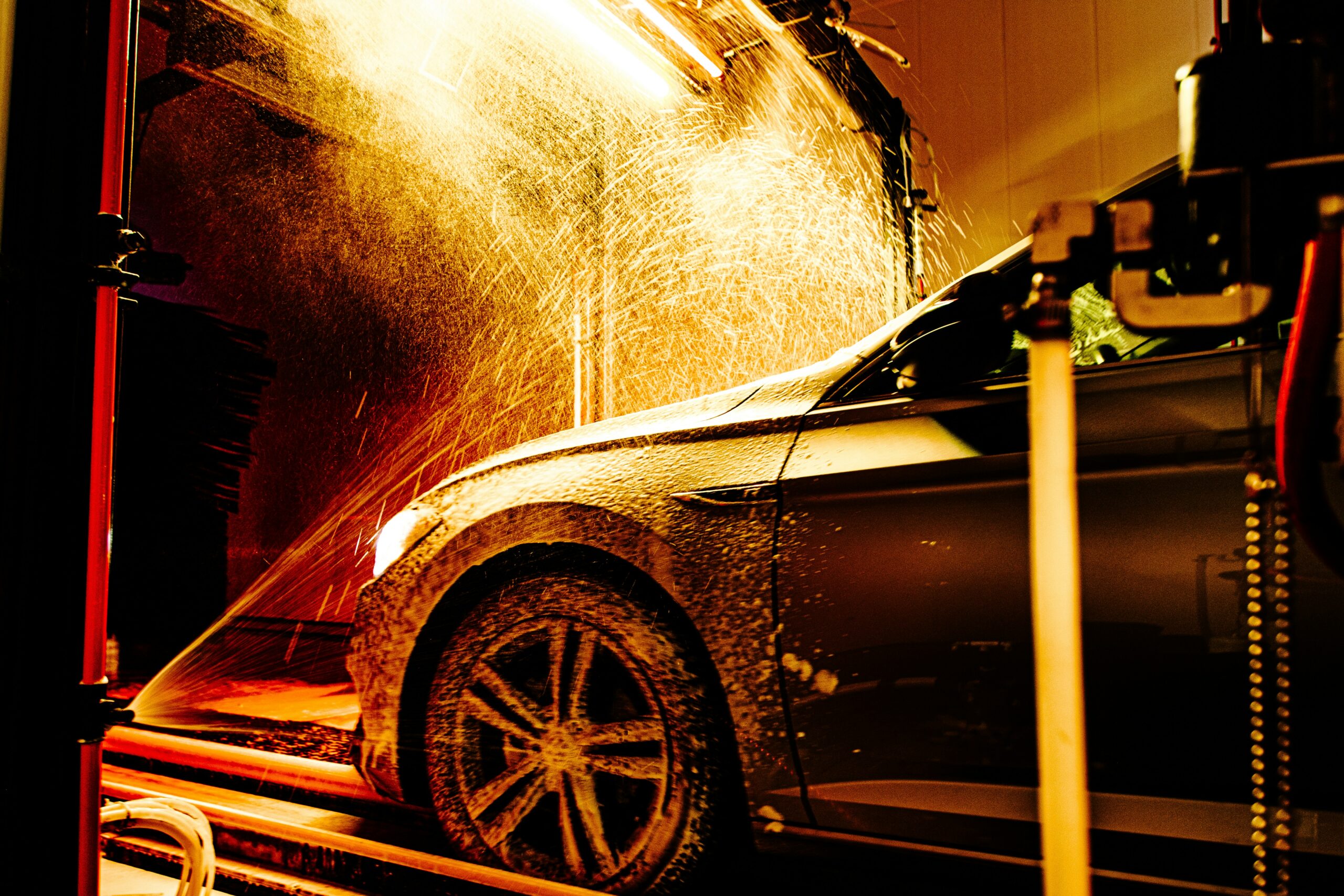 Car going through a car wash tunnel with water spraying from nozzles and blue lighting highlighting the wash process