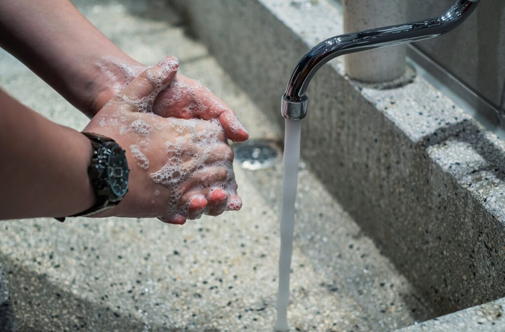 Close-up of hands covered in soap being washed under running water at a sink, highlighting proper hand hygiene and cleanliness.