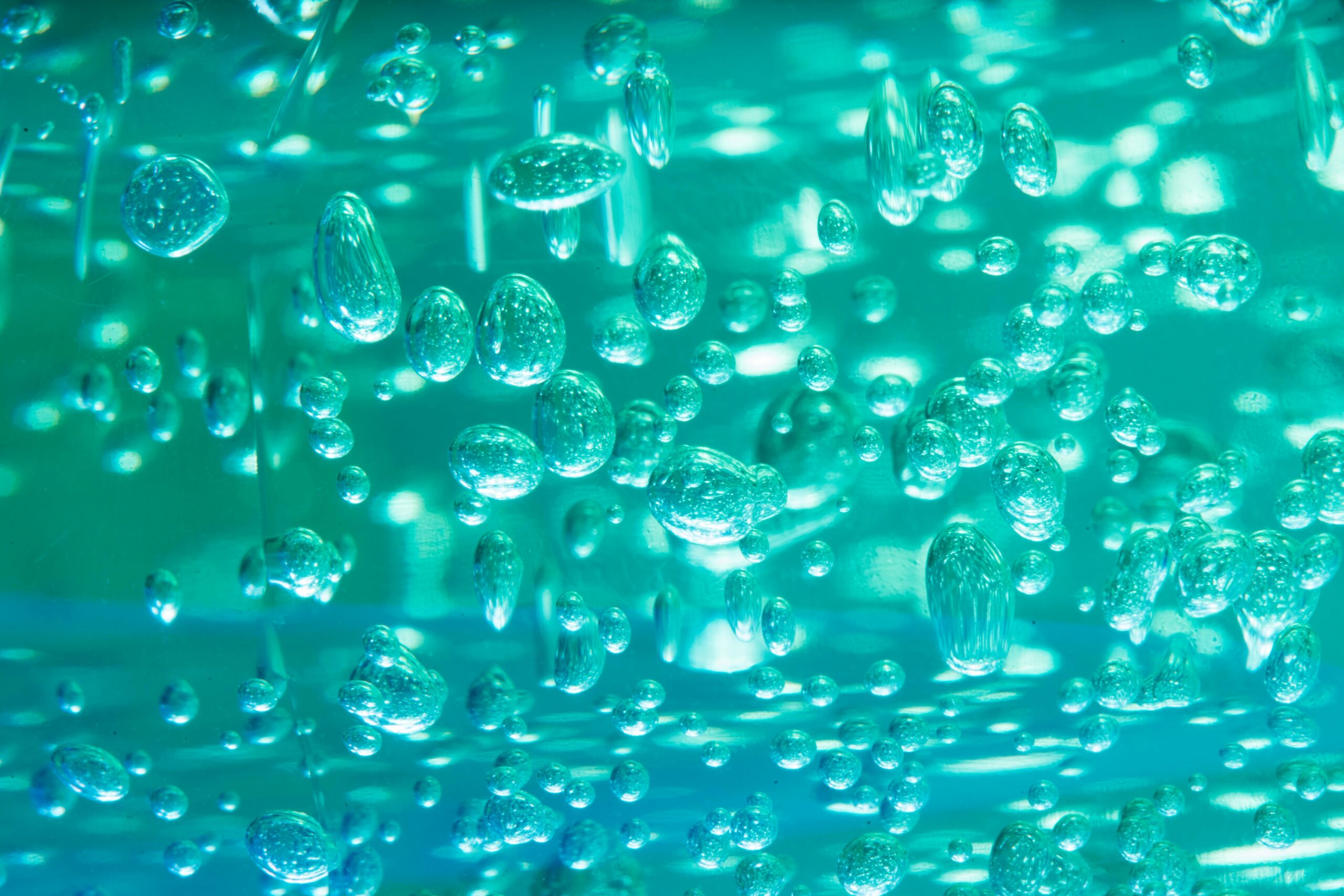 Close-up view of turquoise liquid with suspended air bubbles and glowing reflections, creating an abstract underwater or gel-like texture.