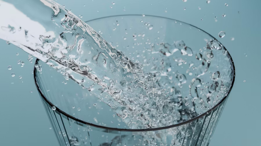 Water splashing into a clear drinking glass against a soft blue background, capturing frozen droplets and motion in high detail.