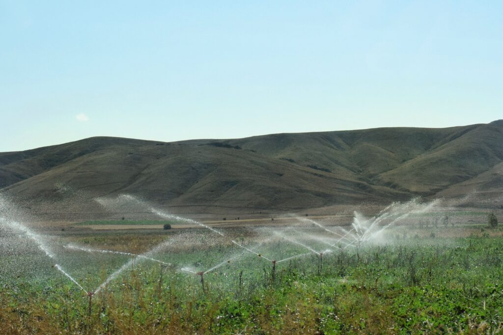 Sprinklers irrigating a green agricultural field beneath rolling hills.
