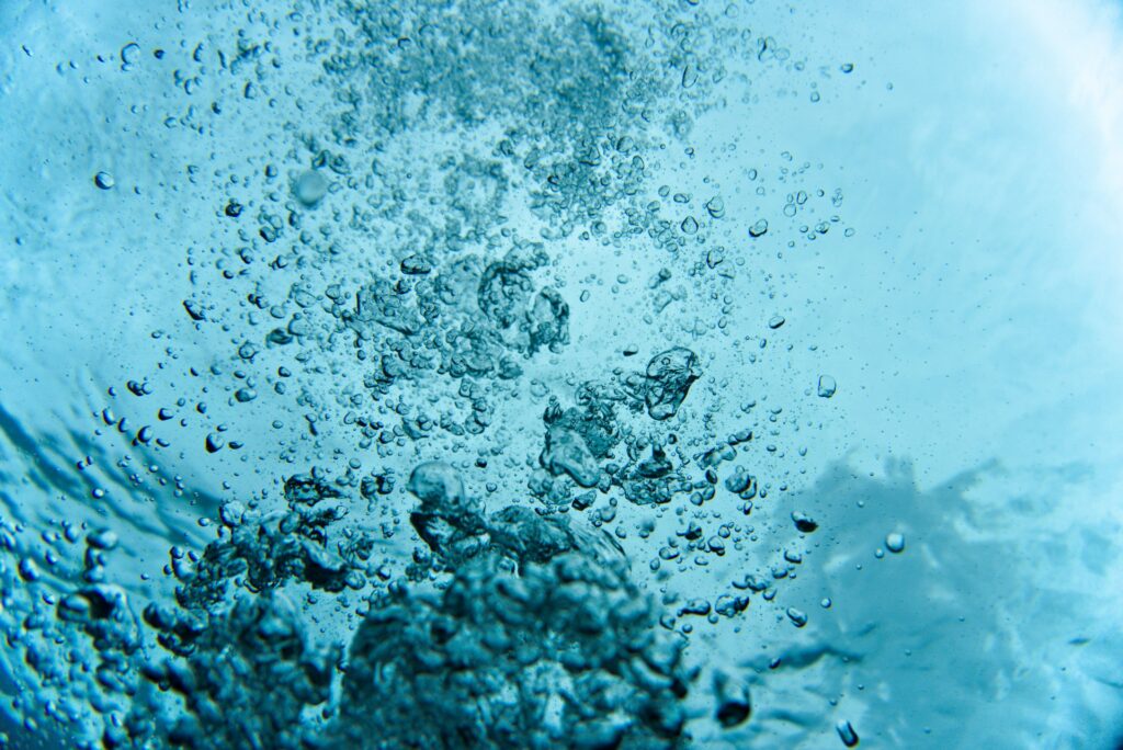 Close-up of air bubbles rising through clear blue water.